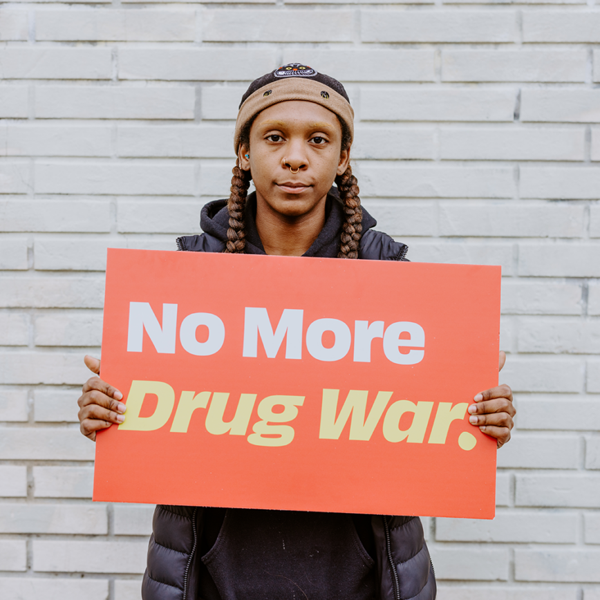 A young woman holds a sign that says "No More Drug War."